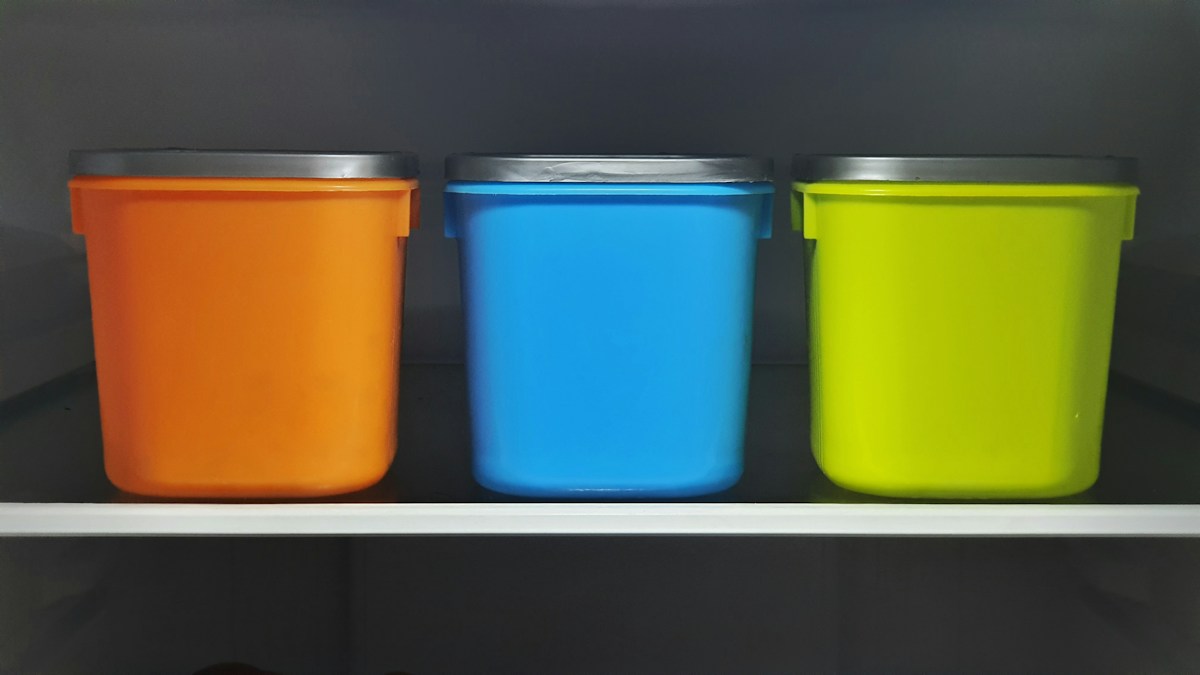 سه سطل پلاستیکی نارنجی، آبی و سبز روی قفسه